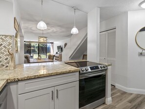 A kitchen with a built-in oven, granite countertop, pendant lights, and a herringbone-patterned wall. - Stunning Kahana Condo Getaway! (Lahaina)