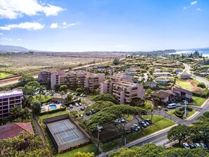 A residential area with multi-story buildings, a tennis court, and a road with vehicles. - Stunning Kahana Condo Getaway! (Lahaina)