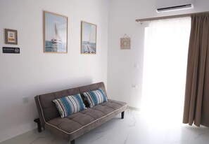 Ein modernes Wohnzimmer mit einem grauen Sofa, zwei gerahmten Bildern, einem Rauchverbot-Schild und einem Fenster mit Vorhängen.