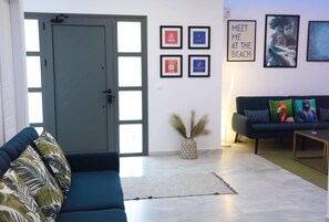 Ein modernes Wohnzimmer mit einem blauen Sofa, einem dunklen Couche und einem Couchtisch. An der Wand hängen gerahmte Bilder und eine Tür mit Glasfenstern.