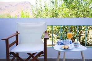 Ein weißer Stuhl und Tisch mit einem Getränk und einem Teller Essen auf einem Balkon mit Blick auf Grünflächen und Berge.