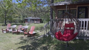 A cabin with a porch, outdoor seating, and a hanging chair. - 3-Bedroom Cottage #1 (Nobel)