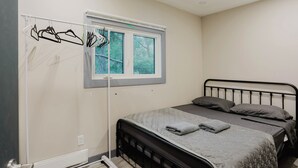 A bedroom with a bed, a window with a view, and a clothes drying rack. - 3-Bedroom Cottage #1 (Nobel)