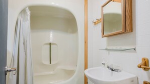 A bathroom with a bathtub, a sink, a mirror, and a shower curtain. - 3-Bedroom Cottage #1 (Nobel)