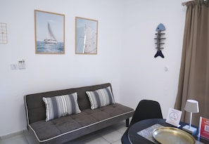 Ein Zimmer mit einem grauen Sofa, zwei gestreiften Kissen, einer Wanddekoration in Fischform und einem gerahmten Bild von einem Segelboot.