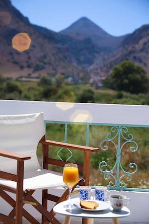 Ein Tisch mit Frühstücksangeboten und einem Glas Orangensaft, mit Blick auf eine gebirgige Landschaft.