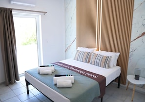Ein Hotelzimmer mit Bett, einer Bank, einem kleinen Tisch und Blick auf Grün durch das Fenster.