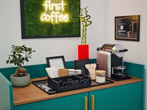 Ein Café mit einem Schild, auf dem 'first coffee' steht, einer Kaffeemaschine, einer Speisekarte und einem Blumentopf.
