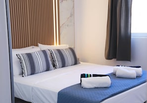 Ein Hotelzimmer mit Bett, Kissen, einer blauen gesteppten Bettdecke und Handtüchern.