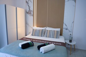 Ein ordentlich bezogenes Bett mit gestreiften Kissen, ein Schild mit der Aufschrift 'SIMPLE ACCOMMODATIONS' und zwei Handtücher auf dem Bett.