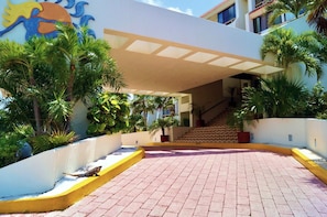 Ein Hotel mit Eingangsbereich, einer überdachten Terrasse, Palmen und einer Treppe zum Gebäude.