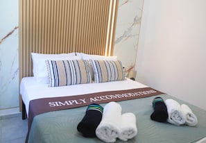 Ein Hotelzimmer mit Bett, Kissen, einem gefalteten Handtuch und einem Schild mit der Aufschrift 'SIMPLY ACCOMMODATIONS'.