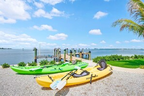Two kayaks on a pebbled beach with a dock and a clear view of the water. - Spacious 4-bedroom Bayfront Home: Dock, Heated Pool, Dolphins and Manatees (Holmes Beach)