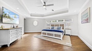 Ein Schlafzimmer mit einem Bett, einem Deckenventilator, einer Kommode, einem Nachttisch und Bildern an den Wänden.