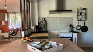 A modern kitchen with a wooden dining table, a gas stove, and a coffee machine. - Villa Nectar ~ Garden ~ Parking ~ Air Conditioning (Beauzelle)