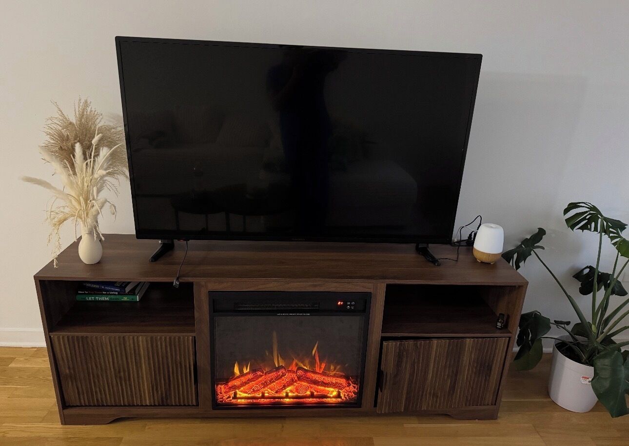 Un meuble de rangement en bois pour appareils multimédias, doté d’un téléviseur à écran plat, d’un foyer intégré et d’une plante en pot.