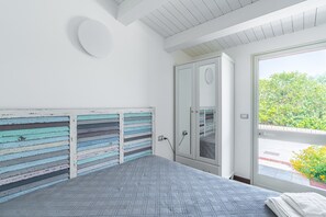 A bedroom with a bed, a window with a view of greenery, a door, and a wall with horizontal stripes. - Room 'Camera Matrimoniale' with Shared Terrace, Wi-Fi and Air Conditioning (Marzamemi)