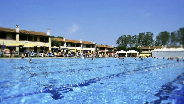 Una piscina con agua cristalina, rodeada de edificios y sombrillas.