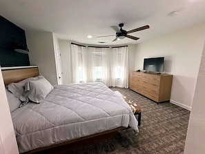 Ein Schlafzimmer mit Bett, Kommode, Fernseher und Deckenventilator.