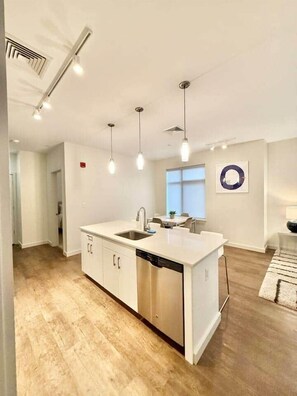 Cozinha moderna com ilha central, eletrodomésticos de aço inoxidável, iluminação pendente e vista para a sala de jantar.