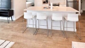 Una cocina moderna con una isla central, taburetes de bar, electrodomésticos de acero inoxidable e iluminación colgante.