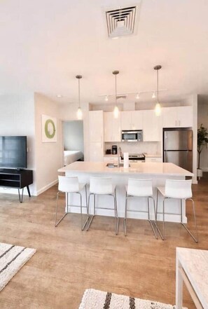 A modern kitchen with a central island, bar stools, stainless steel appliances, and pendant lighting. - The Lumen | Luxury 2BR/2BA | Private Turf Balcony (Cambridge)