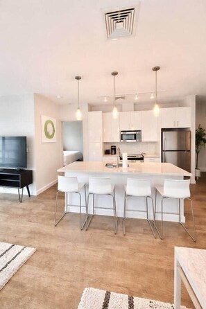 Una cocina moderna con una isla central, taburetes blancos y electrodomésticos de acero inoxidable.