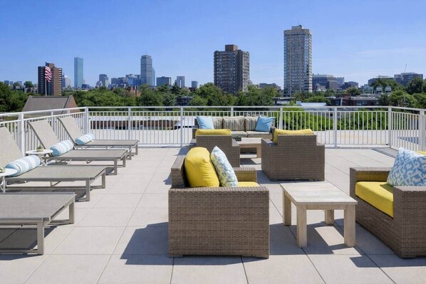Una terraza en la azotea con mobiliario exterior, vistas del horizonte urbano y una valla blanca.
