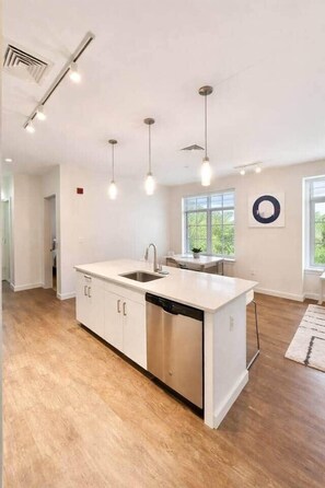 Una cocina moderna con una isla central, electrodomésticos de acero inoxidable, iluminación colgante y ventanas amplias.