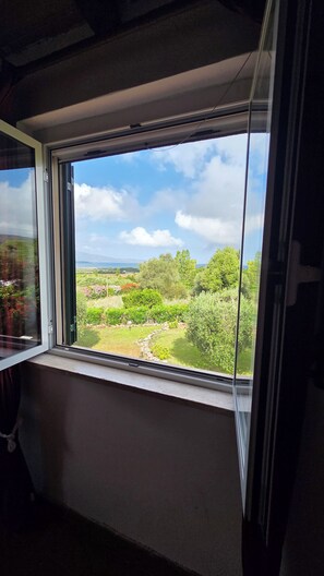 Ein Zimmer mit einem großen Fenster, das einen Blick auf eine Landschaft mit Bäumen und eine ferne Meeransicht bietet.