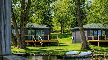 A lakeside cabin with a deck, a small dock, and a grassy area.