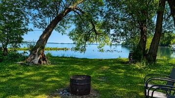 A lakeside setting with a grassy area, a metal barrel, and a bench.