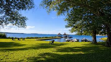 A grassy area with a dock, boats, and a gazebo by a lake.