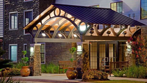 A building with a stone facade, a covered entrance with a curved roof, and large vases in the foreground.