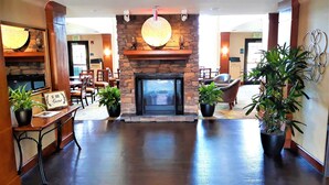 A lobby with a stone fireplace, potted plants, and a sign that reads 'BE OUR GUEST.'