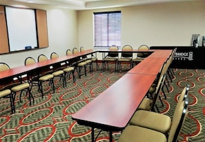 Una sala de conferencias con una mesa larga, sillas, una pantalla de proyector y un ventanal con persianas.