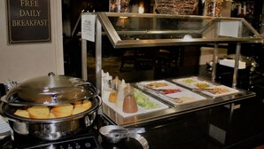 A buffet setup with a sign for free daily breakfast, a variety of food items, condiments, and decorative flowers.