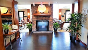 A lobby with a stone fireplace, potted plants, and a sign that reads 'BE OUR GUEST.'