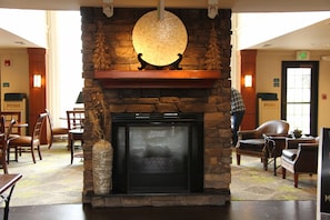 Un hall con chimenea de piedra, sillas de madera, zona de comedor y mostrador de recepción.