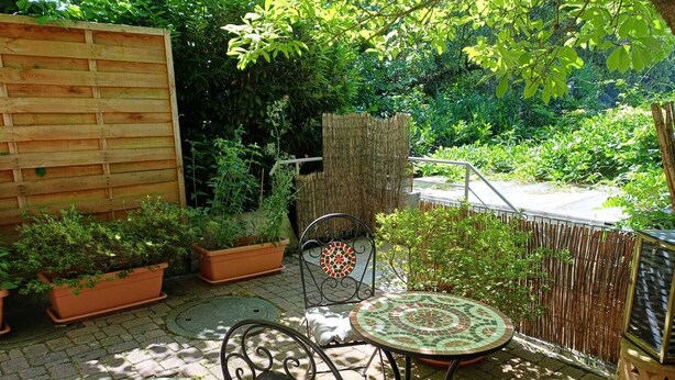 Eine Terrasse mit einem Metallstuhl und Tisch, umgeben von Topfpflanzen und einem Holzzaun.