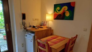 Eine kompakte Küche mit Geschirrspüler, einem Holztisch mit Stühlen, einem farbenfrohen abstrakten Gemälde und einer Tür, die zu einem Außenbereich führt.