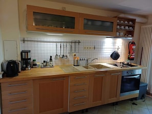 Una cocina con armarios de madera, un lavamanos doble, una cafetera y un extintor.