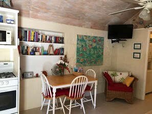 Un comedor con una mesa, sillas, un jarrón con flores, una estantería, un televisor y una obra de arte colgada en la pared.