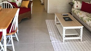 Ein gemütliches Wohnzimmer mit Deckenventilator, einem an der Wand befestigten Fernseher, einem Essbereich mit Tisch und Stühlen sowie einer Couch mit Kissen.