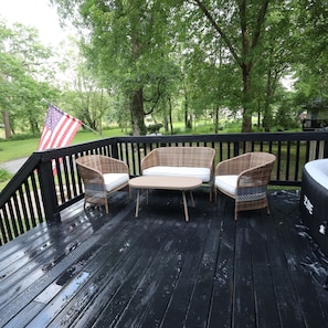 Eine Holzterrasse mit Korbmöbeln, einer US-amerikanischen Flagge und Blick auf eine grüne Landschaft.
