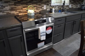 Una cocina con horno de acero inoxidable, hervidor y una toalla colgada en la puerta del horno.