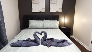 Una cama con colcha estampada, dos obras de arte colgadas en la pared, una lámpara de noche y una decoración de toallas con forma de cisne.