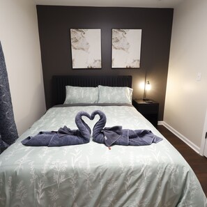 Una cama con colcha estampada, dos obras de arte colgadas en la pared, una lámpara de noche y una decoración de toallas con forma de cisne.