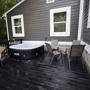 A covered outdoor deck with a hot tub, two chairs, and a small table.