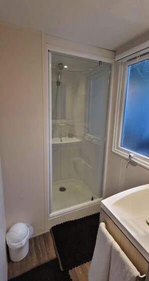 Ein Badezimmer mit einer gläsernen Duschkabine, einem weißen Waschbecken und einem Fenster.